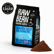 A 200g pack of Raw Bean Definitely Decaf Single Origin coffee next to a pile of coffee grounds in a white studio background with a 2024 Great Taste Award Badge.