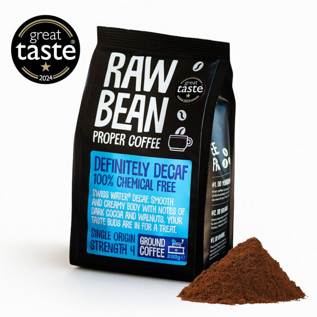 A 200g pack of Raw Bean Definitely Decaf Single Origin coffee next to a pile of coffee grounds in a white studio background with a 2024 Great Taste Award Badge.