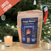 Limited Edition Hygge Haven Dark Roast Ground Coffee from Raw Bean infront of a Christmas tree decorated with sparkling lights.