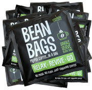 A pile of Relax Revive Go Bean Bags from Raw Bean. These single serve, pyramid coffee bags come with a string and tag and are individually wrapped in recyclable envelopes.