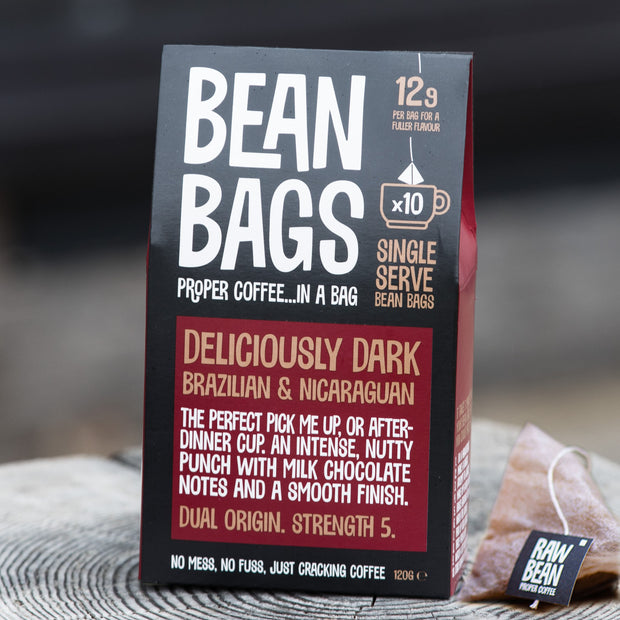 Pack of Deliciously Dark Bean Bags by Raw Bean next to a pyramid coffee bag with string and tag