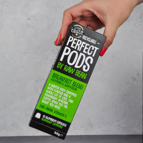 Manicured hand picking up a pack of Raw Bean Perfect Pods Breakfast Blend. 100% Arabica Colombian and Guatemalan coffee blend. 10 Aluminium Capsules Nespresso compatible. 