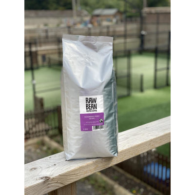 Raw Bean Unpacked Colombian Huila part of the Waitrose Unpacked trial, pack shot on wooden ledge with Padel court in the background 